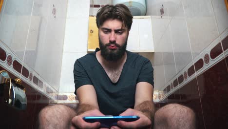 hombre sentado en el baño usando un teléfono inteligente