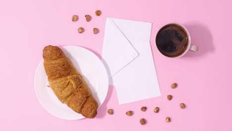 fresh croissant and cup of coffee move around paper card note on pastel pink background. stop motion
