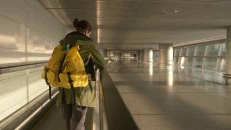 young woman with a yellow backpack in the early morning stands on the escalator at the airport