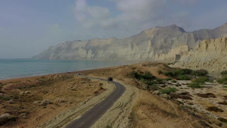 aerial tracking view of 4x4 truck driving along road beside coastline in balochistan