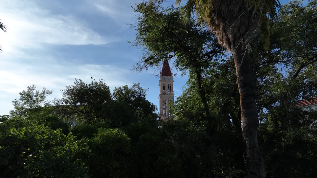 Scenic aerial fly through of lush greenery and palm trees in Trogir, Croatia, to historic tower
