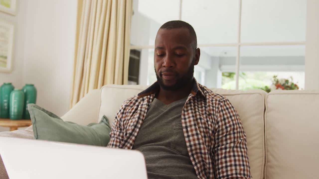 African american man using laptop while sitting on the couch at home