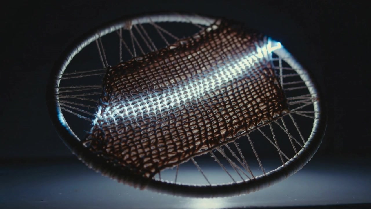 Starting upper-right, narrow light sweeping across hoop with woven mesh in studio, revealing weave