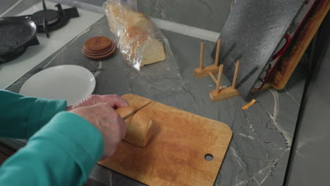 older woman slicing fresh bread on wooden cutting board with a knife, kitchen counter and kitchen tools visible, preparing food at home with modern appliances and cookware