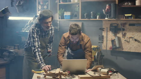 falegnami maschi vecchi e giovani che utilizzano il computer portatile e guardano alcuni video in officina