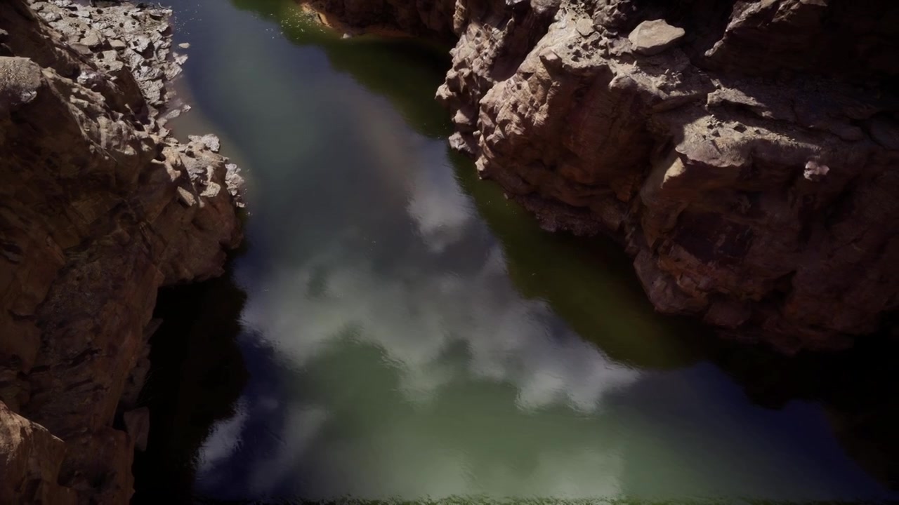 Misteriosos acantilados escarlata encierran un tranquilo embalse verde con nubes suaves.