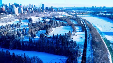 aerial dolly roll over the winter snow cover river valley victoria park with the newly made skating rink oval outdoor with a speed skating race track with the city of edmonton in the background sunny