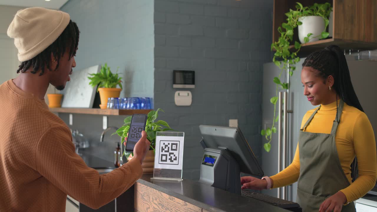 African American man showing smartphone QR code at counter while barista processing payment on till