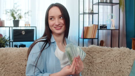 young woman happily counting pile of cash dollar bills on sofa celebrating wealth successful finance