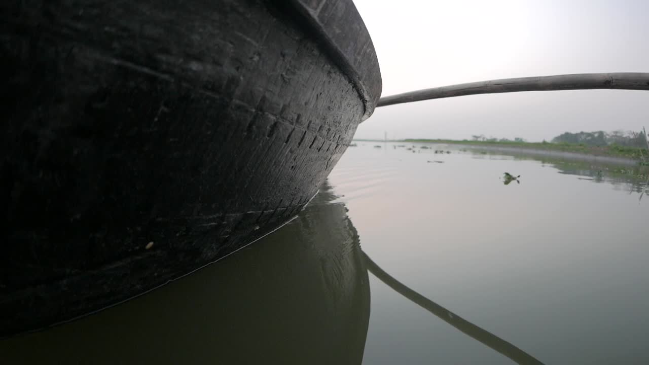 Side of a small boat cruising through the dirty backwaters of Bangladesh.