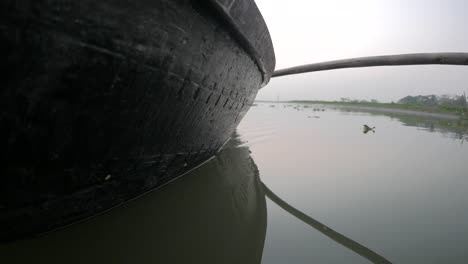 side of a small boat cruising through the dirty backwaters of bangladesh.