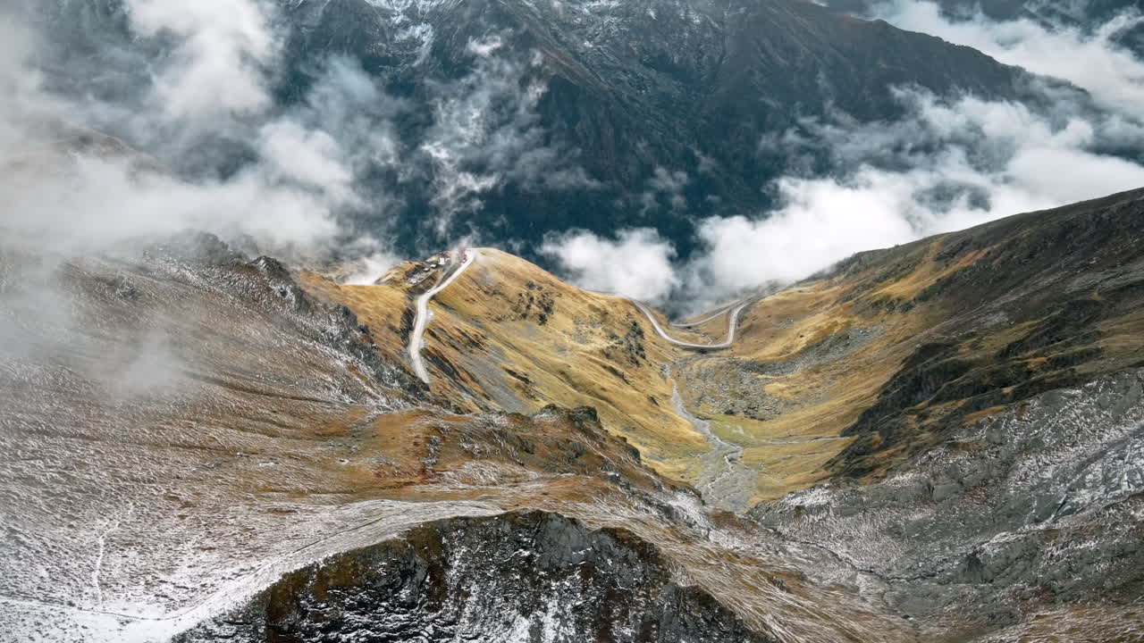 Aerial drone view of nature in Romania. Transfagarasan route in Carpathian mountains, snow on mountains rocky slopes, valley, clouds