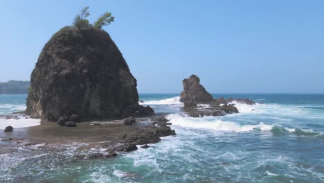 Vista-Aérea-De-Olas-Espumosas-Rompiendo-En-Un-Islote-Rocoso-En-La-Costa-De-Watu-Lumbung-En-Indonesia