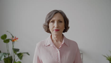 senior woman with gray hair and white shirt looking at camera with serious expression