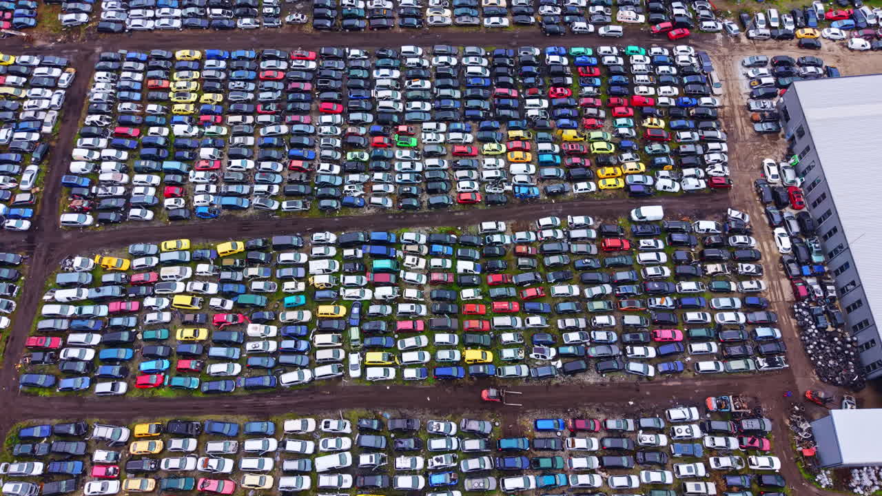 Gran cantidad de coches estacionados en un depósito de vehículos, vistos desde arriba en un día soleado con cielo despejado en una concurrida zona urbana.