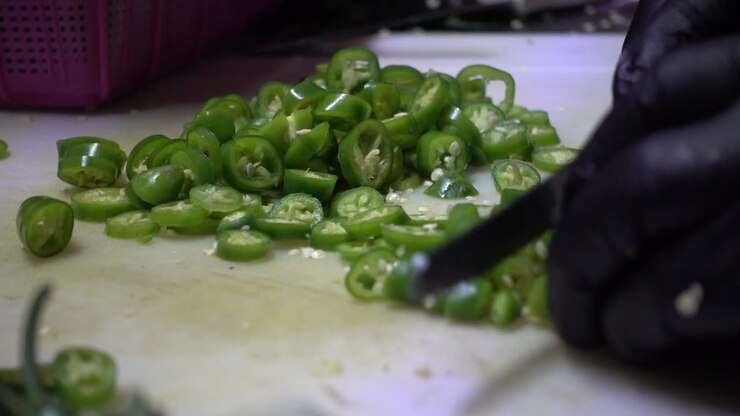 Close-up shot of a chef using a knife to slice up jalapeno peppers on a chopping board