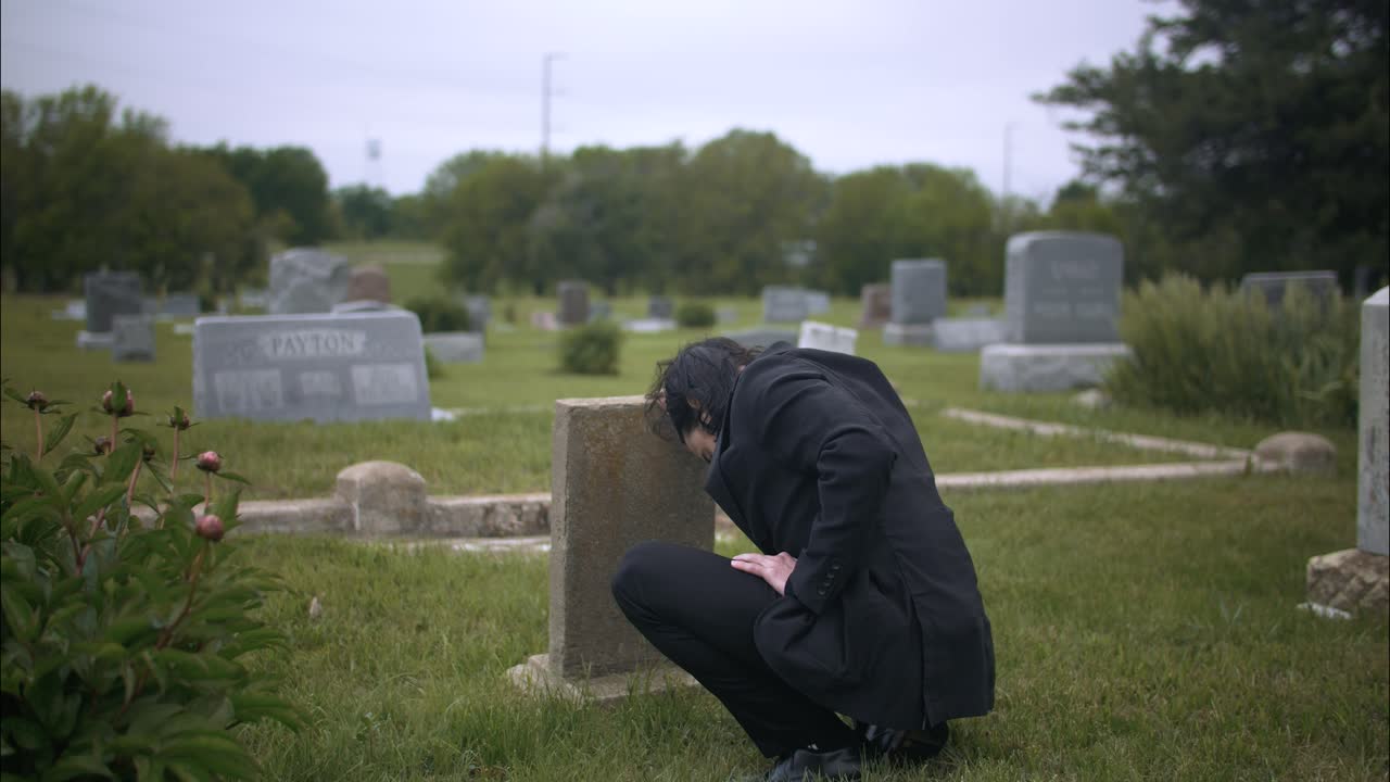 Man mourning over death of loved one at grave tombstone in cemetery