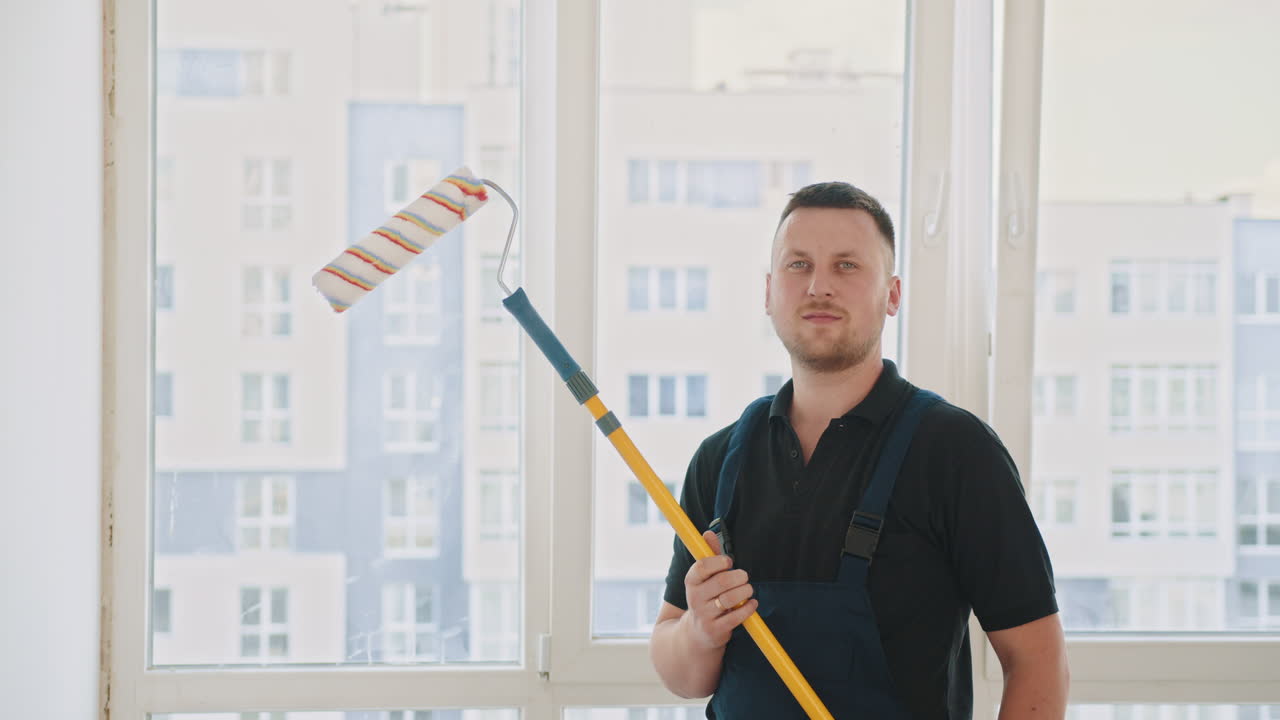pintor sosteniendo un rodillo de pintura cerca de la ventana