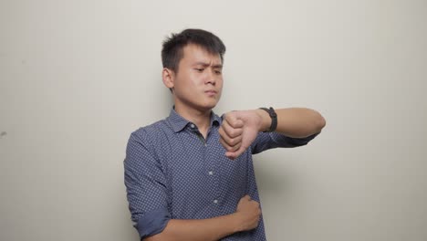 studio shot of young asian man waiting impatiently watching clock in blue shirt