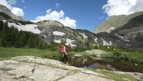 young female hiker with backpack walking by scenic glacial lake on sunny summer day