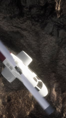 un helicóptero blanco con acentos rojos vuela sobre un terreno rocoso.