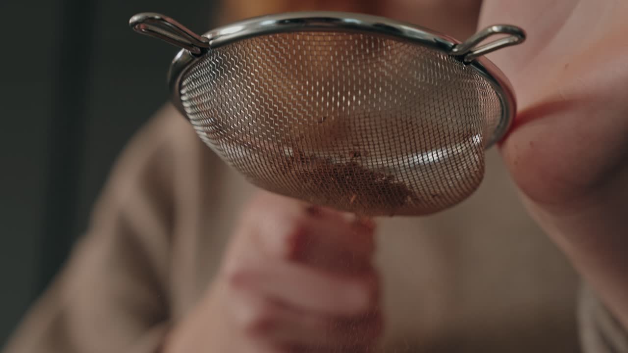 Slow motion cocoa powder falling through sieve by hand