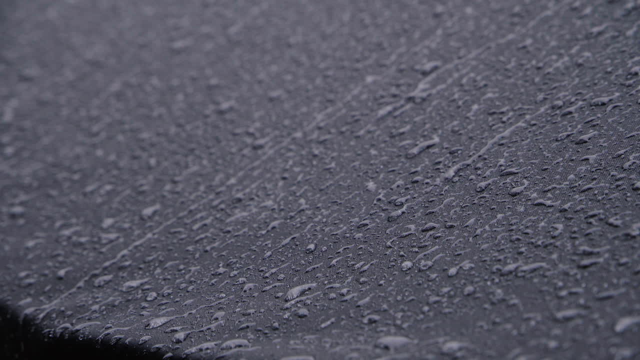 fuertes lluvias sobre textiles impermeables negros. 4k