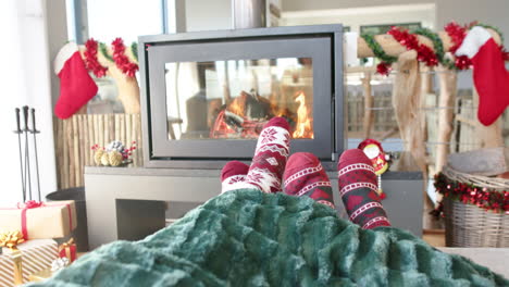 feet of diverse gay male couple on sofa by fireplace at home at christmas, slow motion