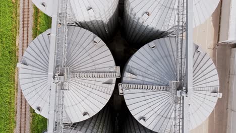smooth backward aerial shot of silver grain silos in latvia under cloudy sky