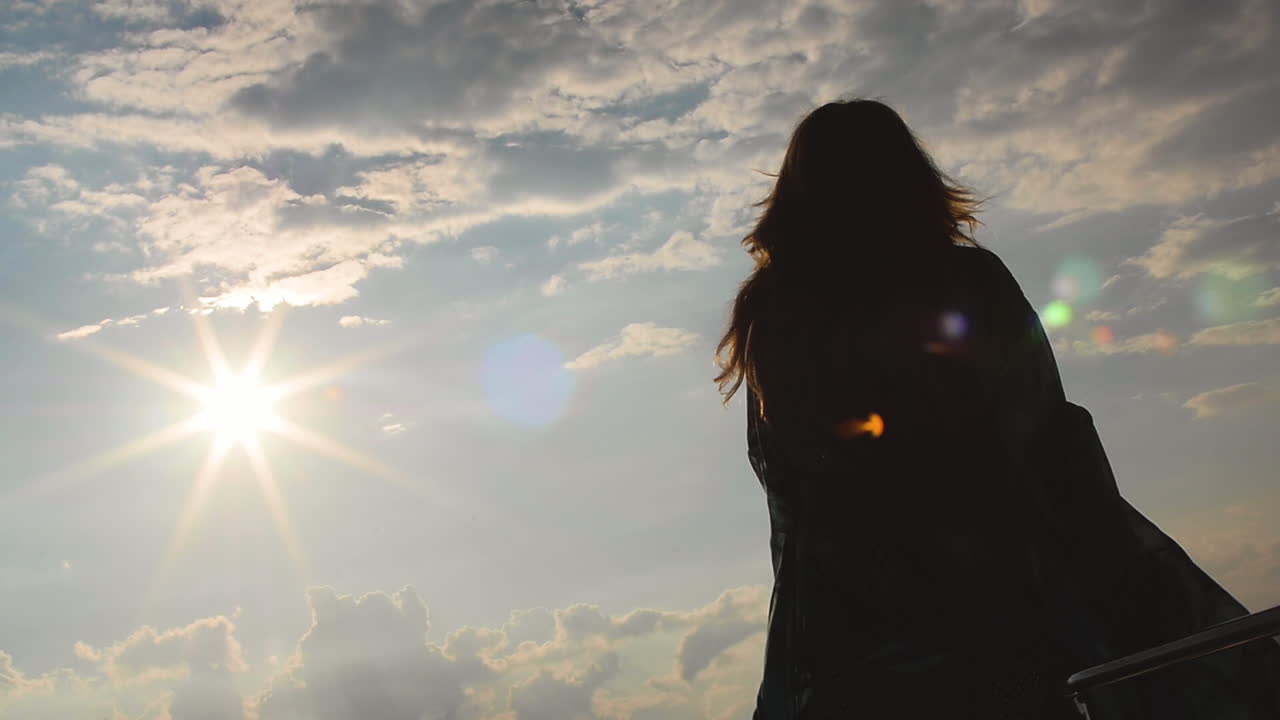 a Woman in a long flowing dress dances by herself in the sunshine. Her figure is silhouetted with beauty. She celebrates life and happiness in her femininity