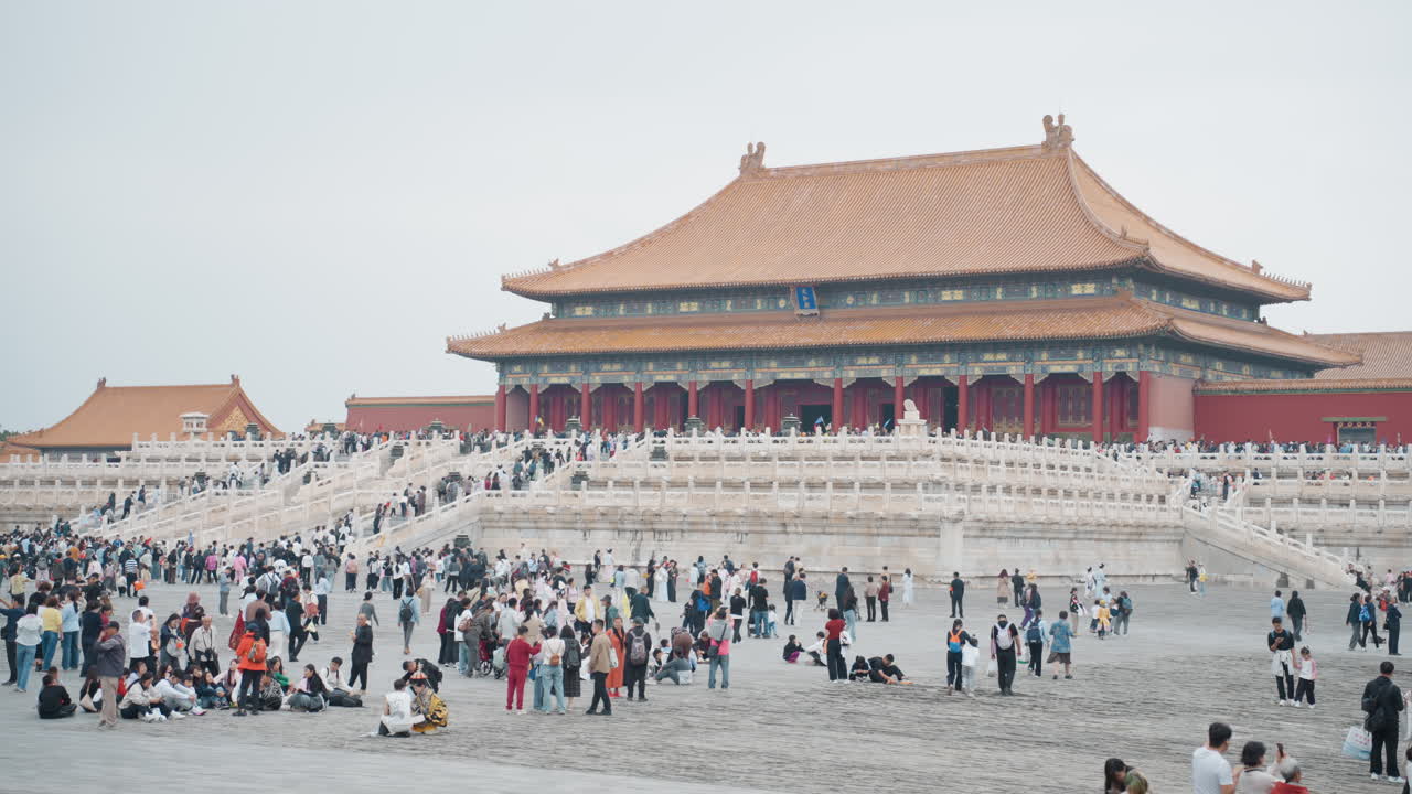 Cortile affollato della Città Proibita: turisti asiatici, fotografi, famiglie, guide salgono i gradini di marmo verso il palazzo imperiale rosso sotto un cielo coperto; un'ampia composizione cattura la scala e l'eredità culturale.