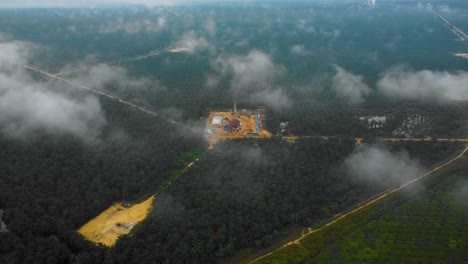 Cinematic-Drone-Shot-of-Onshore-Drilling-and-Workover-Rig-structure-and-Rig-equipment-for-oil-exploration-and-exploitation-in-the-middle-of-jungle-surrounded-by-palm-oil-trees-during-sunset-time