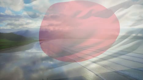 composición digital de la bandera de japón ondeando contra la vista aérea de la playa y las olas del mar