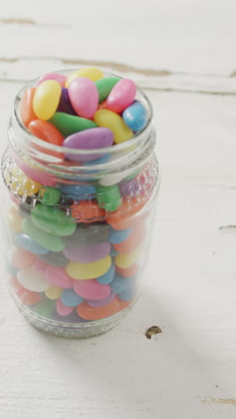 video of overhead view of multi coloured jelly sweets in jar over white rustic background