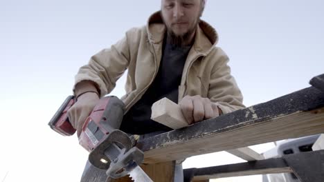 male carpenter cuts through wood with reciprocating saw outside, low angle shot