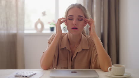 Tired-woman-sits-by-closed-laptop-at-white-table-in-office