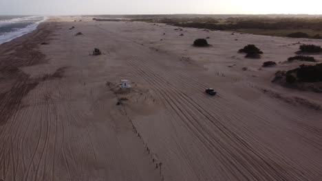vista aérea del camión de cuatro ruedas que sale de la playa y conduce por un camino forestal rural junto a las olas de agua de la playa en américa del sur, argentina