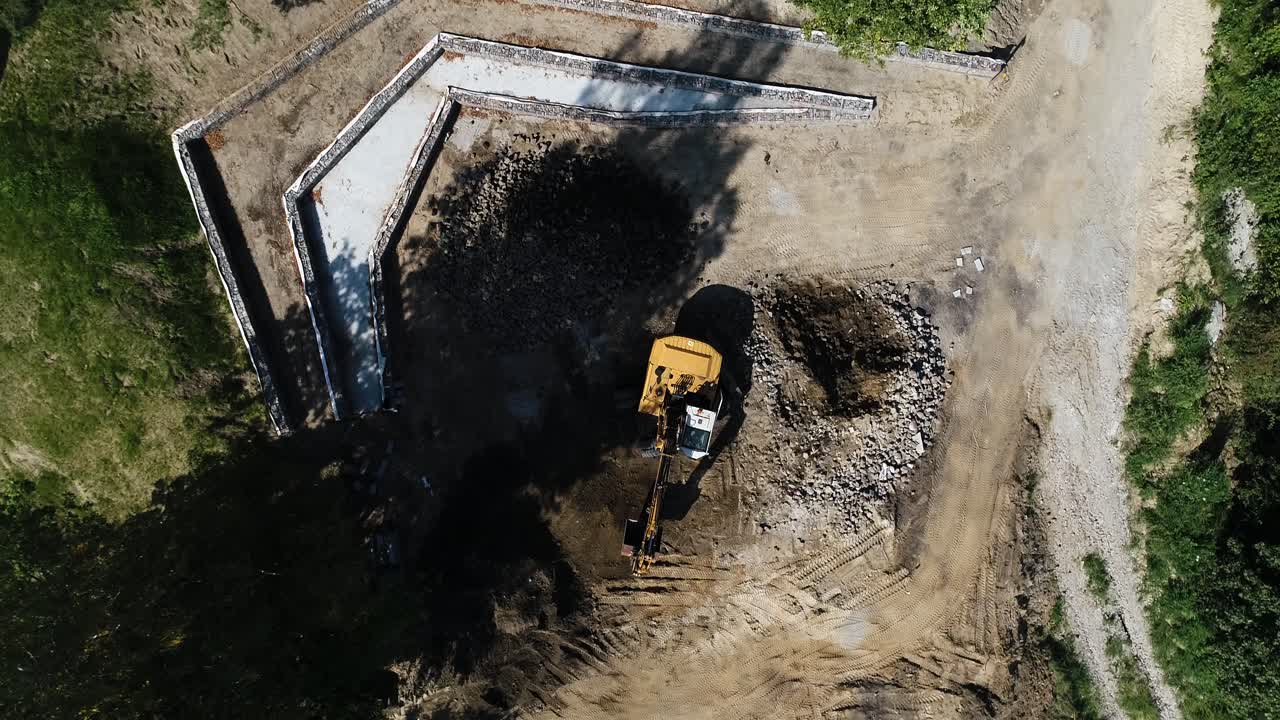 vista aérea de arriba hacia abajo de un camión excavadora que trabaja en un sitio de construcción de área remota para construir un distrito residencial en un entorno natural
