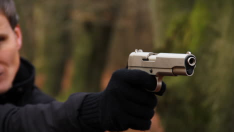 primer plano de un criminal disparando una pistola en un bosque