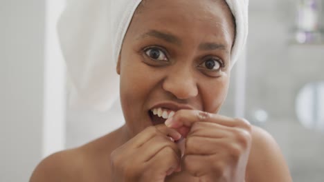 Happy-african-american-woman-flossing-teeth-and-using-smartphone-in-bathroom