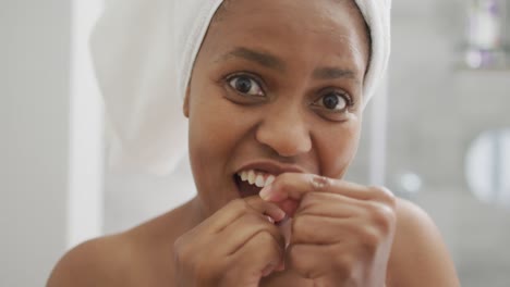 happy african american woman flossing teeth and using smartphone in bathroom