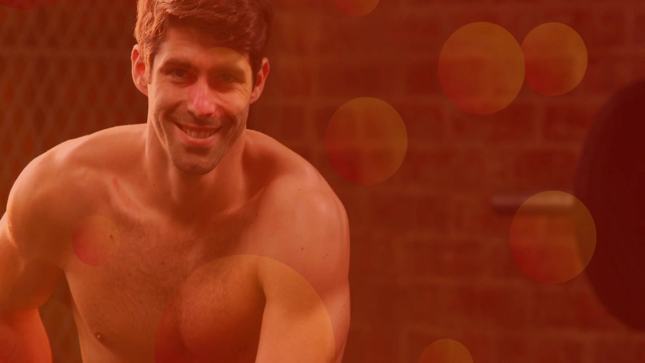 Uomo inginocchiato che sistema i pantaloncini in palestra, riscaldandosi mentre il bokeh mostra un kettlebell intorno a lui.