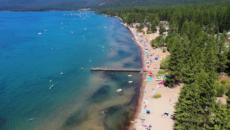 vista aérea de personas relajándose en una playa de arena rodeada por un bosque de pinos en el lago tahoe