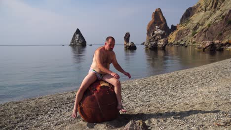 hombre haciendo ejercicio al aire libre cerca de una vieja mina marina flotante oxidada en la playa con orilla rocosa y fondo marino. estilo de vida saludable, contaminación, protección de la naturaleza, concepto de guerra y paz