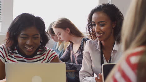 woman teacher giving one to one support to female student working at desk on laptop