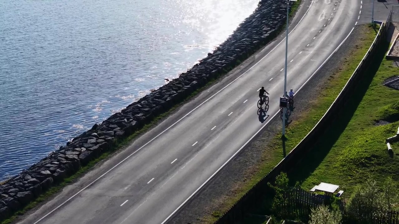Dois ciclistas pedalam em ciclovia à beira-mar passando por um quebra-mar de pedra, Reykjavík, Islândia