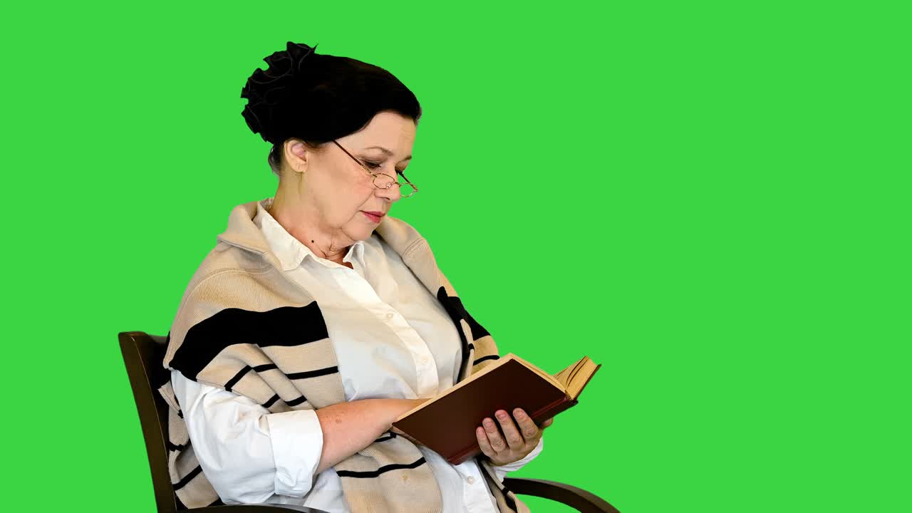 mujer mayor amigable sentada en una silla leyendo un libro en una pantalla verde, llave de croma