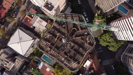 aerial straight down shot showing industrial construction site on rooftop of extreme high skyscraper building in downtown - orbit shot