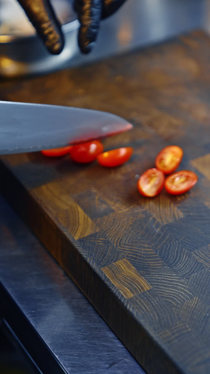 Male cook wearing black gloves cutting little tomatoes into halves. Preparing food concept. Close up. Vertical video.