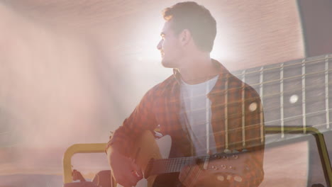 animation of lights over happy caucasian man playing guitar on beach